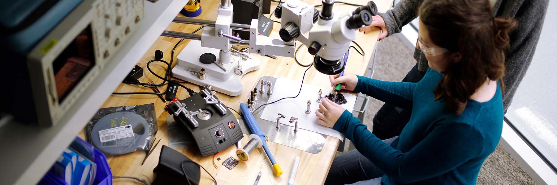 Students use magnifying equipment in a lab to solder together a prototype.