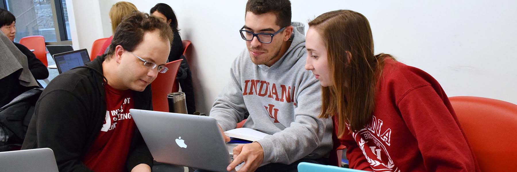 Three students look at a laptop as they work together on a group project during class.